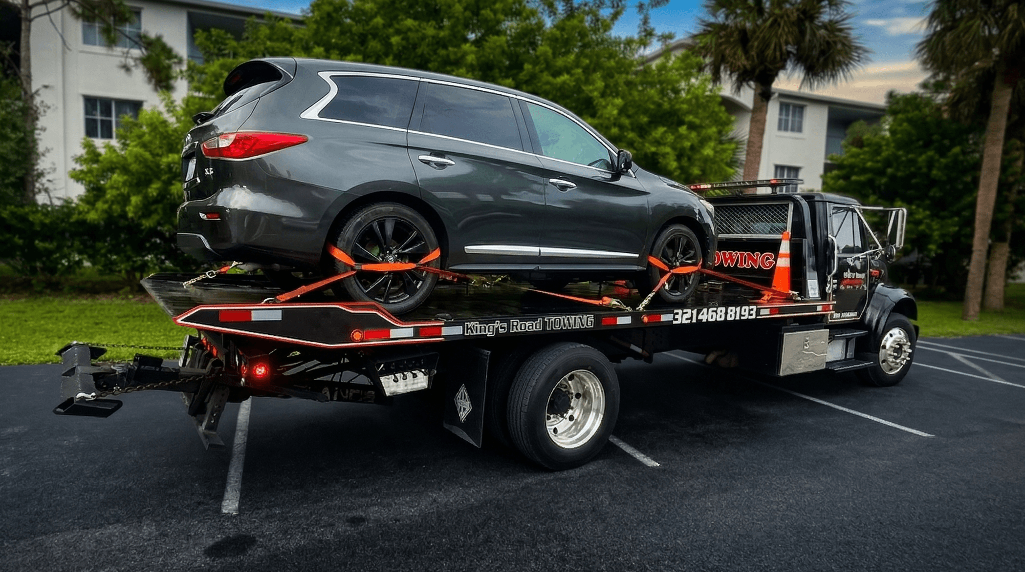 Worker securing car with straps on flatbed tow truck